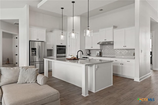 kitchen with dark wood finished floors, tasteful backsplash, stainless steel appliances, under cabinet range hood, and white cabinets