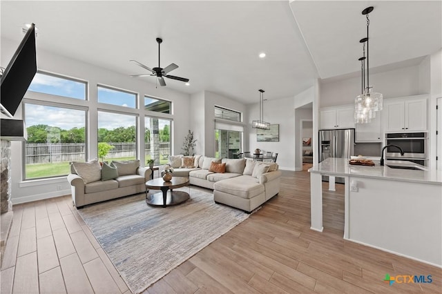 living room with baseboards, light wood-type flooring, ceiling fan, and plenty of natural light