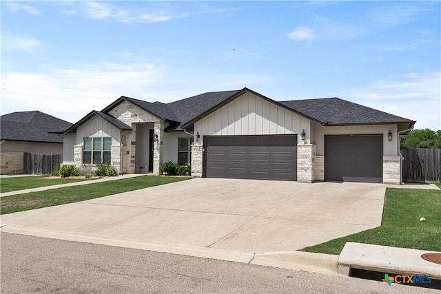 view of front of home with concrete driveway, stone siding, fence, a front lawn, and a garage