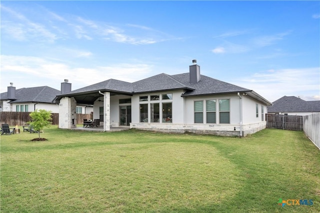 back of property featuring a chimney, a patio area, a shingled roof, a lawn, and a fenced backyard