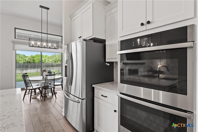 kitchen featuring light stone counters, white cabinetry, tasteful backsplash, light wood-style flooring, and appliances with stainless steel finishes