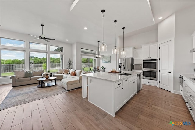 kitchen featuring light wood-style flooring, a sink, appliances with stainless steel finishes, ceiling fan, and open floor plan