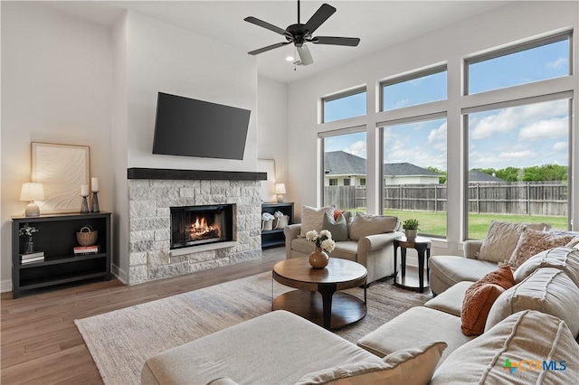 living room featuring a towering ceiling, ceiling fan, wood finished floors, and a fireplace
