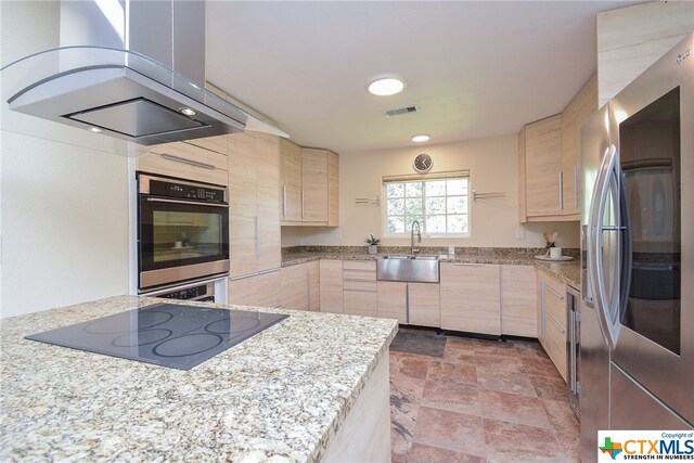 kitchen with light stone counters, appliances with stainless steel finishes, exhaust hood, light brown cabinets, and sink