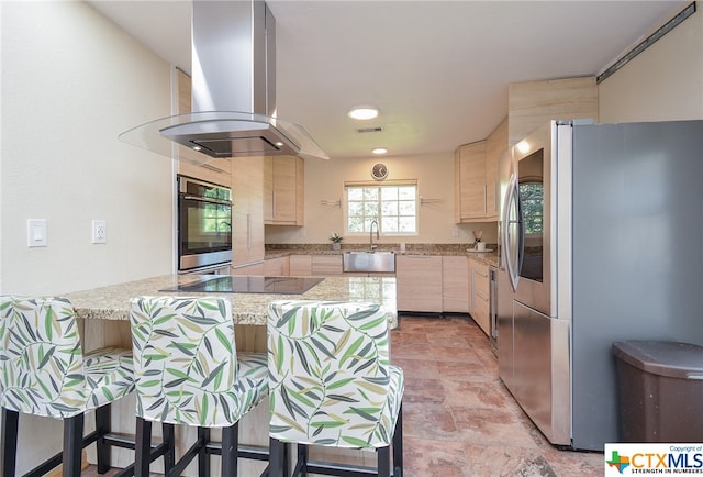 kitchen with island range hood, light stone counters, stainless steel appliances, a kitchen breakfast bar, and kitchen peninsula