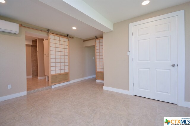 basement with a barn door, light tile patterned floors, and a wall mounted air conditioner