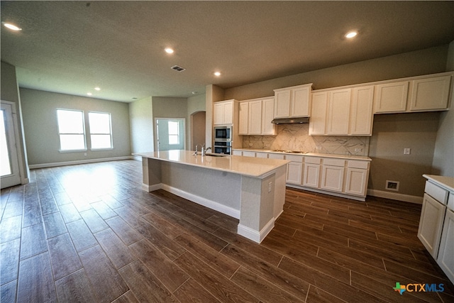 kitchen with dark wood-type flooring, white cabinetry, appliances with stainless steel finishes, and an island with sink