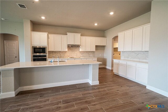 kitchen with a kitchen island with sink, decorative backsplash, dark hardwood / wood-style flooring, and white cabinets