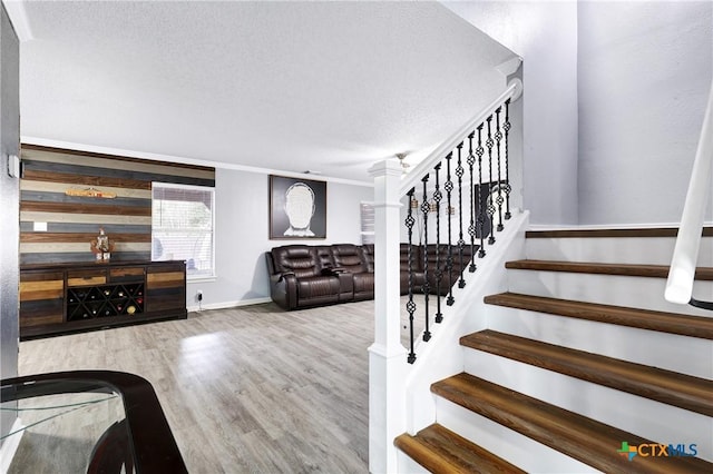 stairs with ornamental molding, wood-type flooring, and a textured ceiling