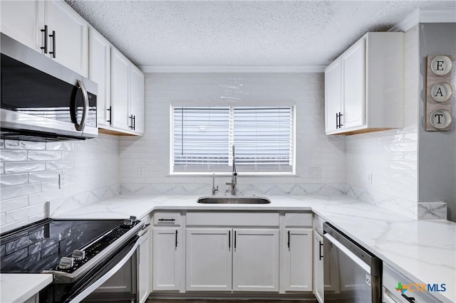 kitchen with appliances with stainless steel finishes, sink, white cabinets, backsplash, and light stone counters