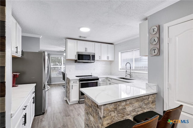 kitchen with white cabinetry, sink, ornamental molding, kitchen peninsula, and stainless steel appliances