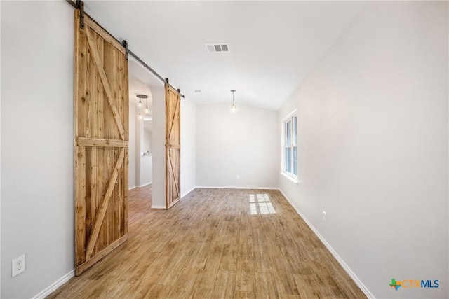 empty room featuring visible vents, lofted ceiling, a barn door, light wood finished floors, and baseboards