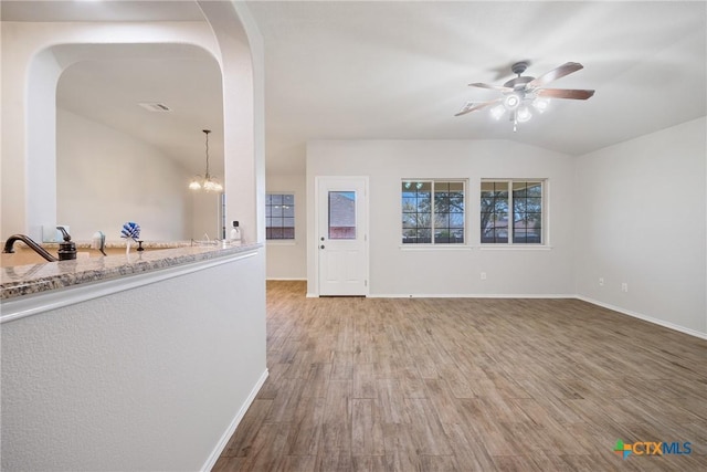 interior space with visible vents, vaulted ceiling, ceiling fan with notable chandelier, wood finished floors, and arched walkways