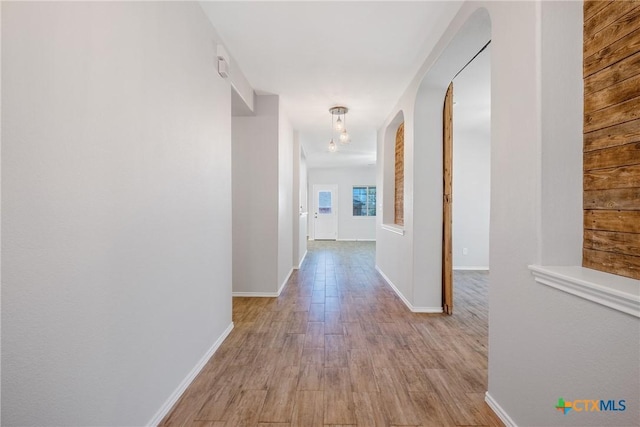 hallway with baseboards, arched walkways, and light wood finished floors