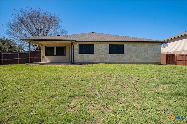 back of house with a yard, stone siding, roof with shingles, and fence