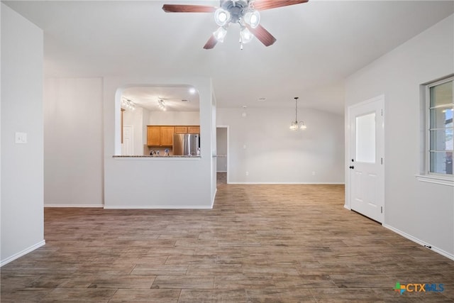 unfurnished living room with wood finished floors, ceiling fan with notable chandelier, baseboards, and vaulted ceiling