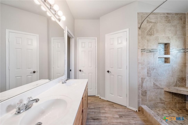 full bath featuring double vanity, a tile shower, and a sink