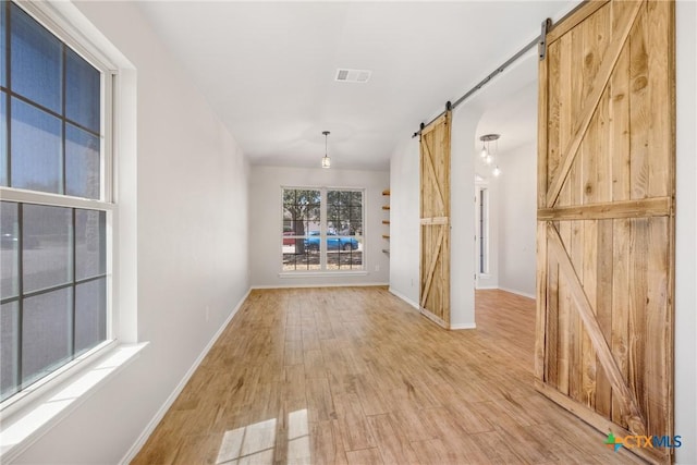 unfurnished room featuring visible vents, baseboards, light wood-type flooring, and a barn door