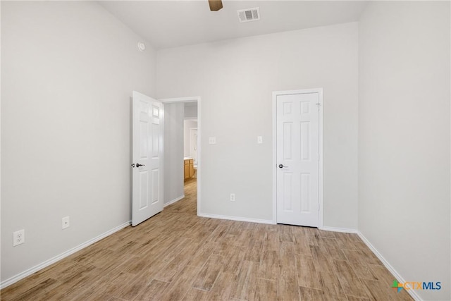 unfurnished bedroom with a ceiling fan, visible vents, baseboards, a towering ceiling, and light wood-type flooring