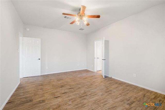 empty room with ceiling fan, visible vents, baseboards, and wood finished floors