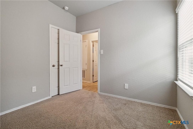 empty room with a healthy amount of sunlight, baseboards, and light carpet