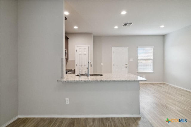 kitchen featuring visible vents, a sink, light wood finished floors, and light stone counters