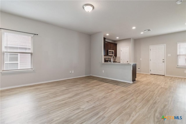 unfurnished living room with a sink, recessed lighting, baseboards, light wood-type flooring, and visible vents