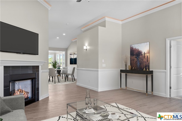 living room featuring hardwood / wood-style flooring, ornamental molding, a tile fireplace, and vaulted ceiling