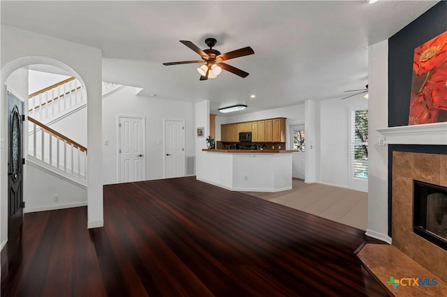 unfurnished living room with a tiled fireplace, wood-type flooring, and ceiling fan