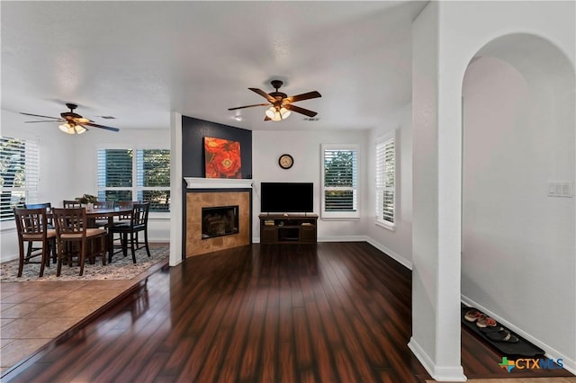 living room featuring a tile fireplace, dark hardwood / wood-style floors, a wealth of natural light, and ceiling fan