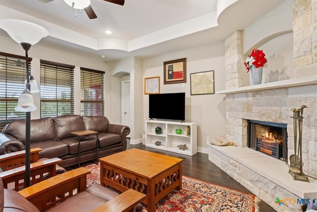 living room featuring ceiling fan, a stone fireplace, a raised ceiling, and hardwood / wood-style flooring