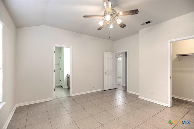 unfurnished bedroom featuring a walk in closet, a closet, vaulted ceiling, ceiling fan, and light tile patterned floors