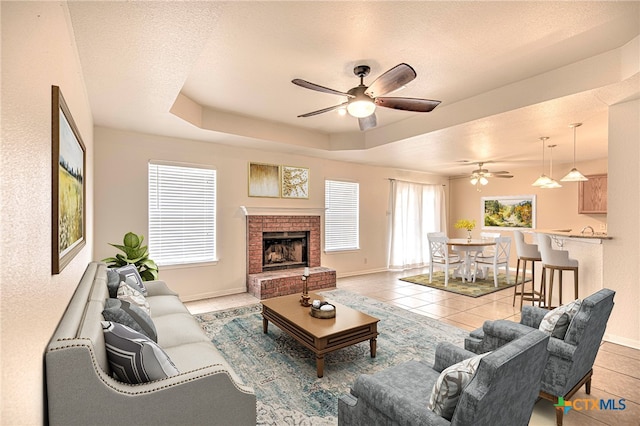 living room with a textured ceiling, light tile patterned flooring, ceiling fan, and a raised ceiling