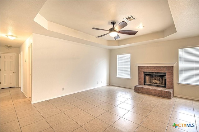 unfurnished living room with a textured ceiling, ceiling fan, a fireplace, a tray ceiling, and light tile patterned floors