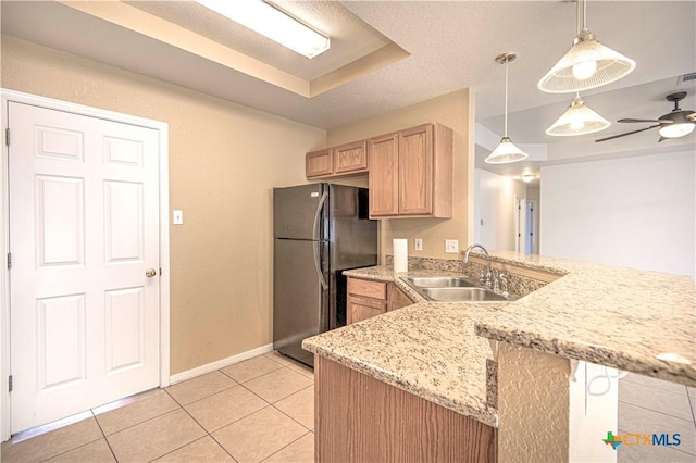 kitchen featuring sink, black fridge, decorative light fixtures, light brown cabinetry, and kitchen peninsula