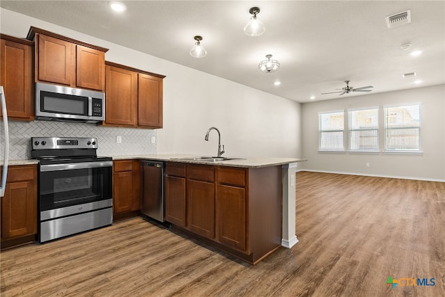 kitchen with hardwood / wood-style flooring, kitchen peninsula, appliances with stainless steel finishes, and sink