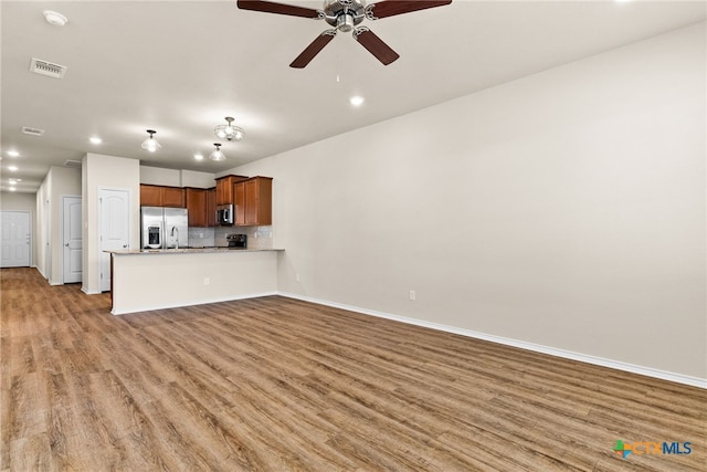 kitchen featuring stainless steel appliances, light hardwood / wood-style floors, kitchen peninsula, decorative backsplash, and ceiling fan