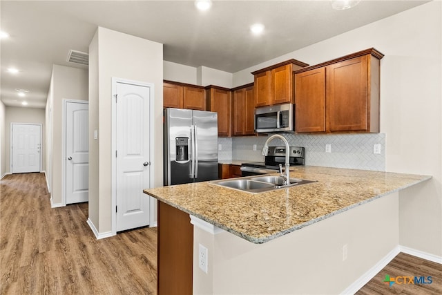 kitchen with decorative backsplash, kitchen peninsula, wood-type flooring, and stainless steel appliances