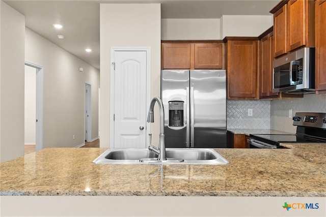 kitchen with tasteful backsplash, light stone countertops, appliances with stainless steel finishes, and sink