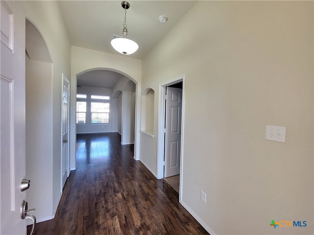 corridor with arched walkways, dark wood finished floors, and baseboards