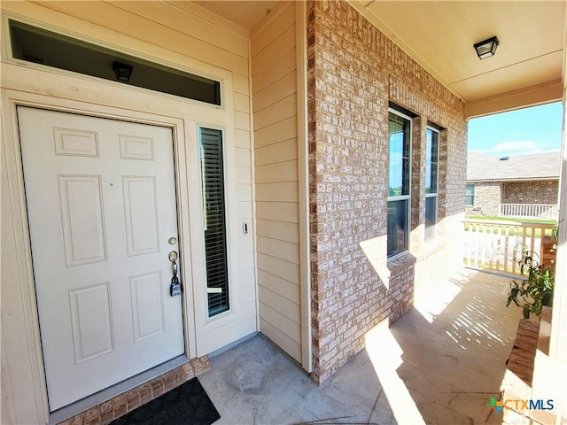 property entrance featuring covered porch and brick siding