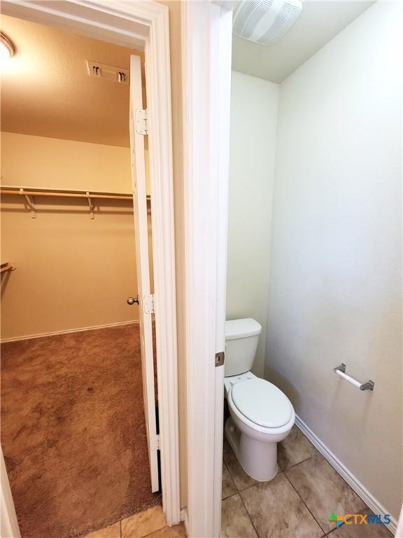 bathroom with tile patterned flooring, toilet, visible vents, baseboards, and a walk in closet