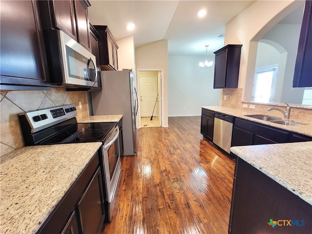 kitchen with dark wood-style floors, stainless steel appliances, vaulted ceiling, a sink, and light stone countertops