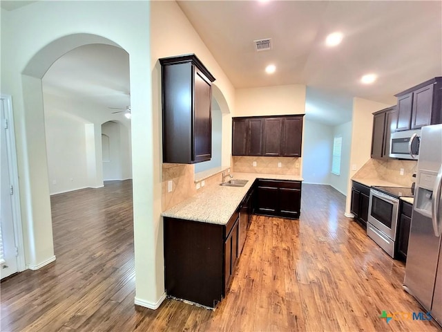 kitchen featuring arched walkways, stainless steel appliances, a sink, visible vents, and light wood-type flooring