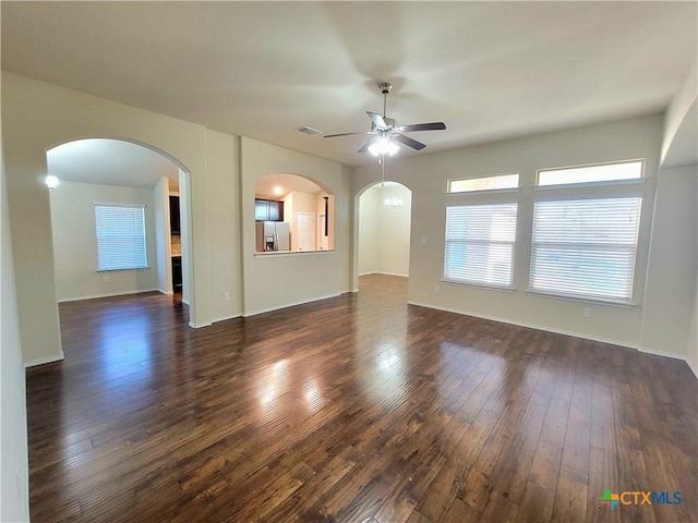 unfurnished room with a ceiling fan, arched walkways, visible vents, and dark wood finished floors