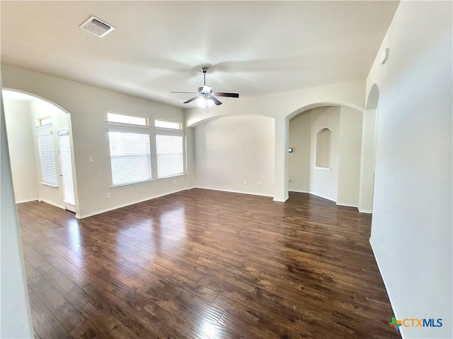 empty room featuring arched walkways, dark wood finished floors, visible vents, a ceiling fan, and baseboards