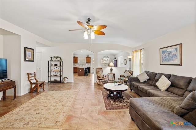 living area featuring light tile patterned floors, arched walkways, and ceiling fan with notable chandelier