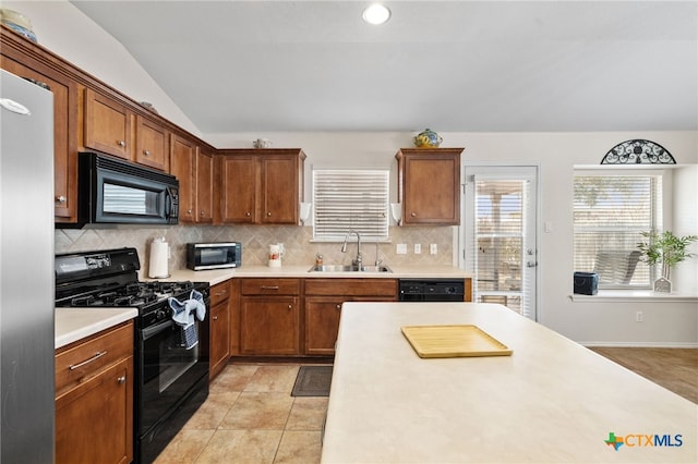 kitchen featuring lofted ceiling, a sink, black appliances, light countertops, and backsplash