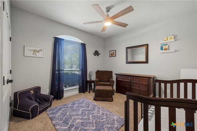 carpeted bedroom featuring ceiling fan and a nursery area