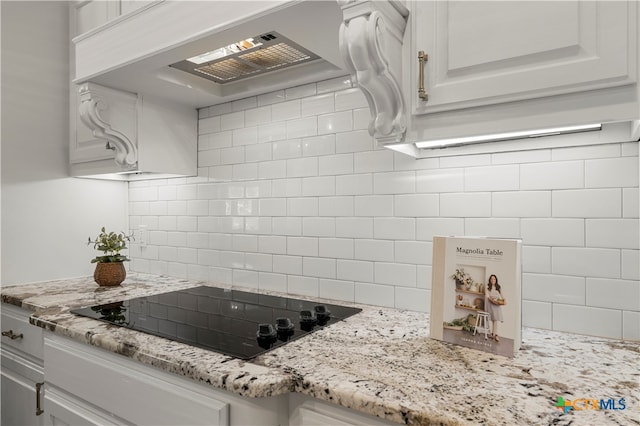 kitchen featuring light stone countertops, custom exhaust hood, white cabinets, black electric stovetop, and decorative backsplash